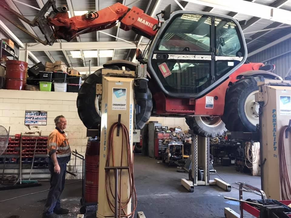 A Man is Standing Next to a Tractor in a Garage — Drinnan's Diesel & Automotive Repairs In Gladstone Central, QLD