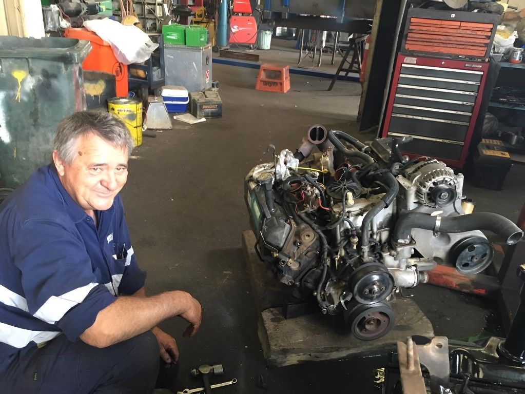 A Man is Kneeling Next to a Engine in a Garage — Drinnan's Diesel & Automotive Repairs In Gladstone Central, QLD