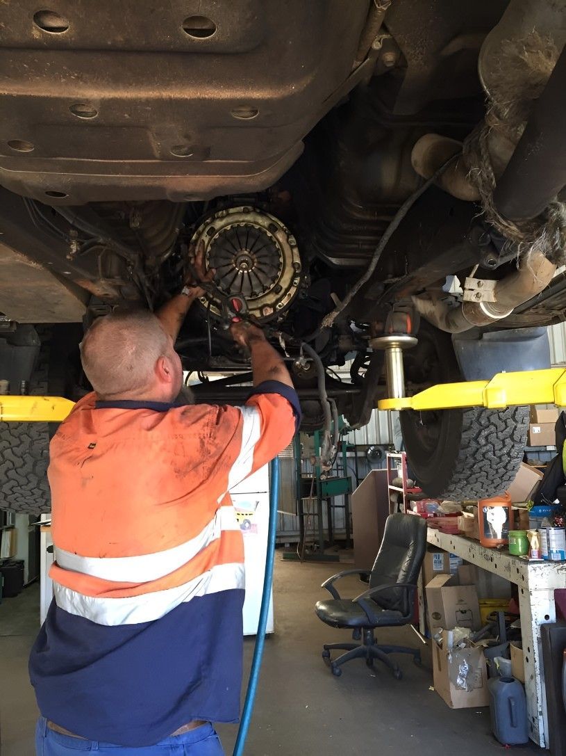 A Man is Working Under a Car in a Garage — Drinnan's Diesel & Automotive Repairs In Gladstone Central, QLD