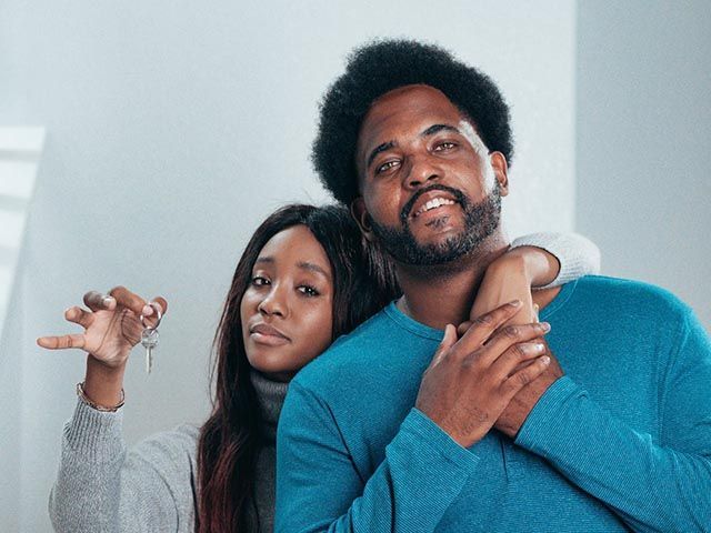a-smiling-couple-standing-close-together-with-the-woman-holding-up-a-set-of-house-keys