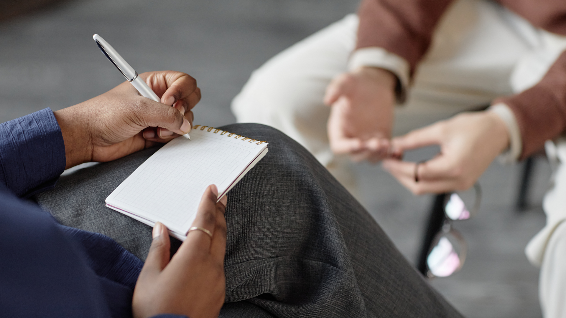 Person taking notes during a consultation. A notepad and pen are visible, as are the other person’s hands.