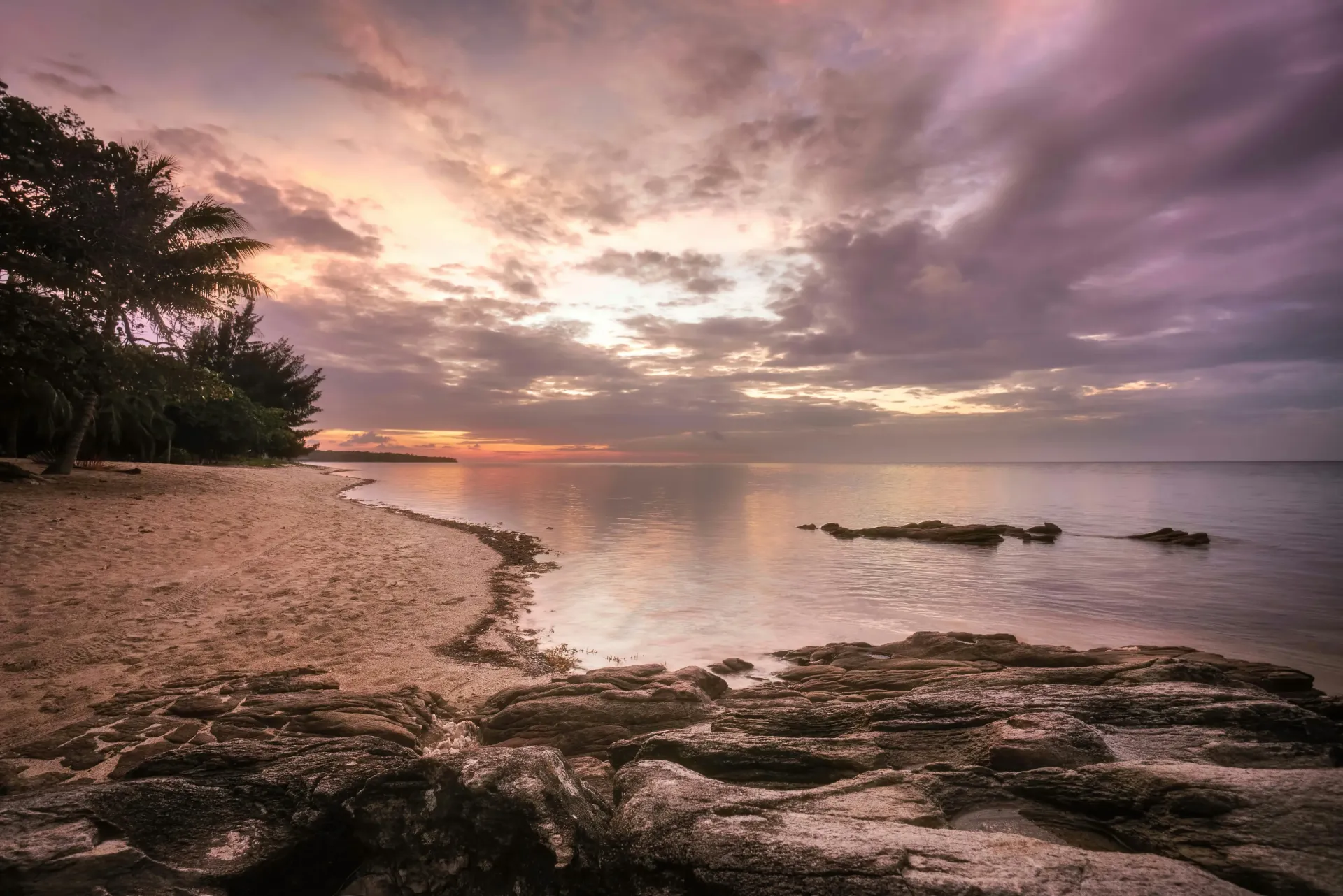 Una puesta de sol sobre una playa con rocas y árboles.
