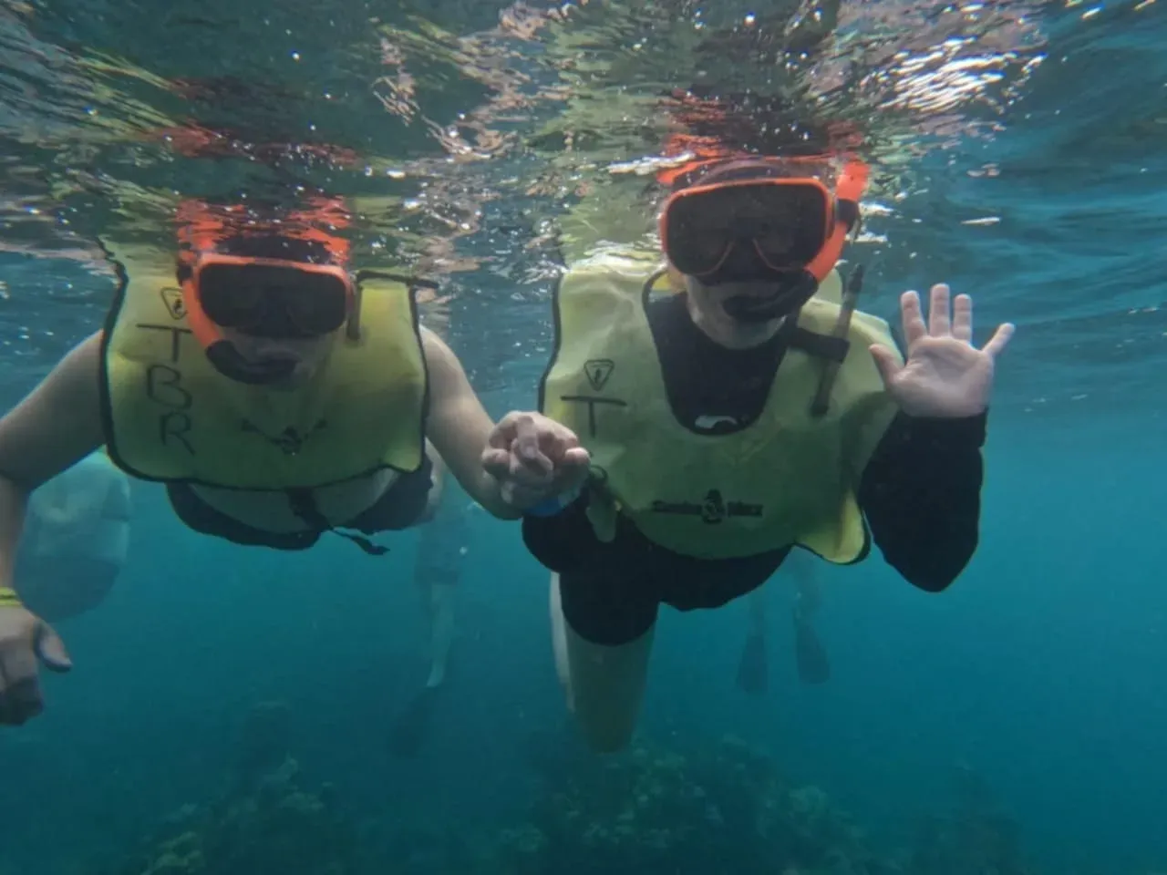 Two people wearing life vests and goggles are swimming in the ocean