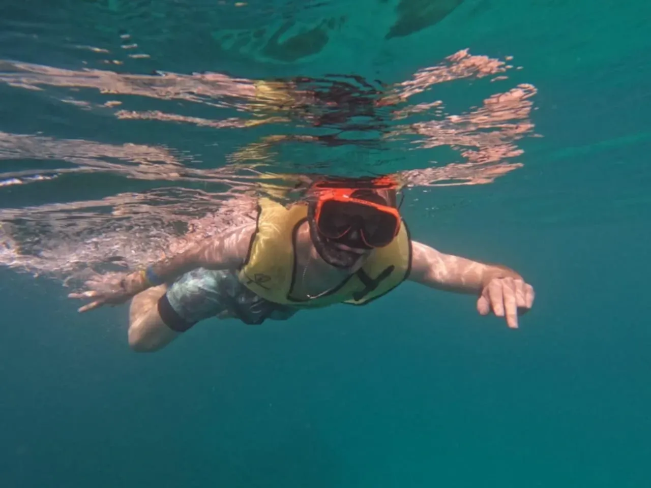 A person is swimming underwater in a life jacket and mask.