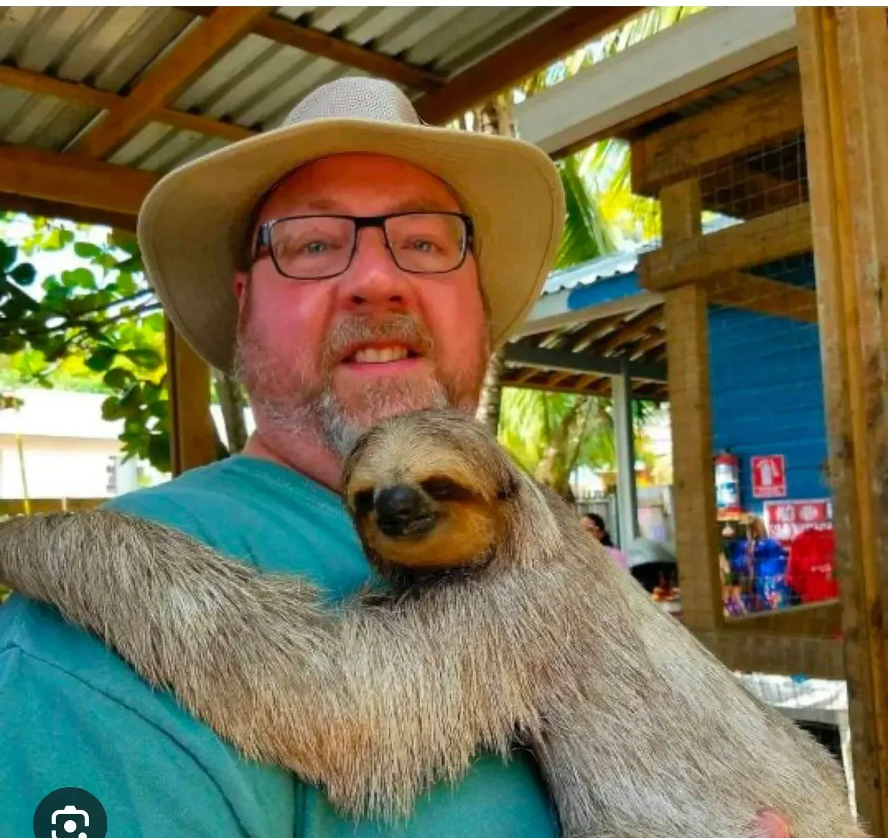 Un hombre con sombrero y gafas sostiene un perezoso.