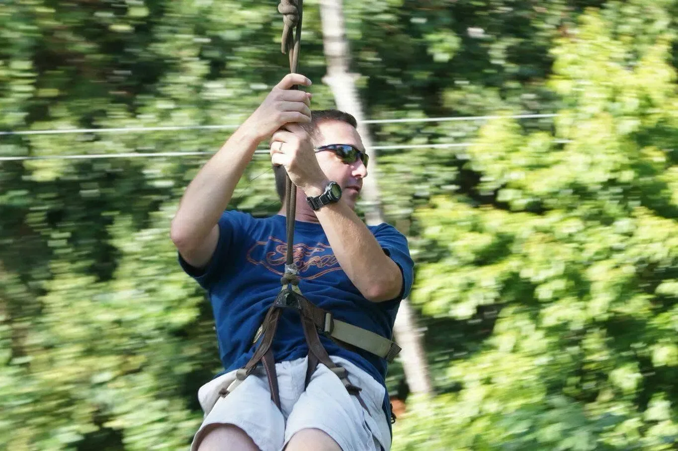 A man is riding a zip line in the woods.