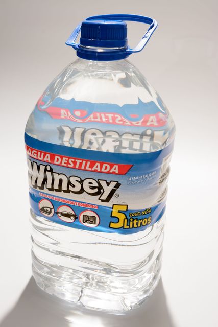 Jarra de agua de plástico con tapa y asa azules, etiquetada con las palabras “Winsey” y “Agua Destilada” en rojo y azul.