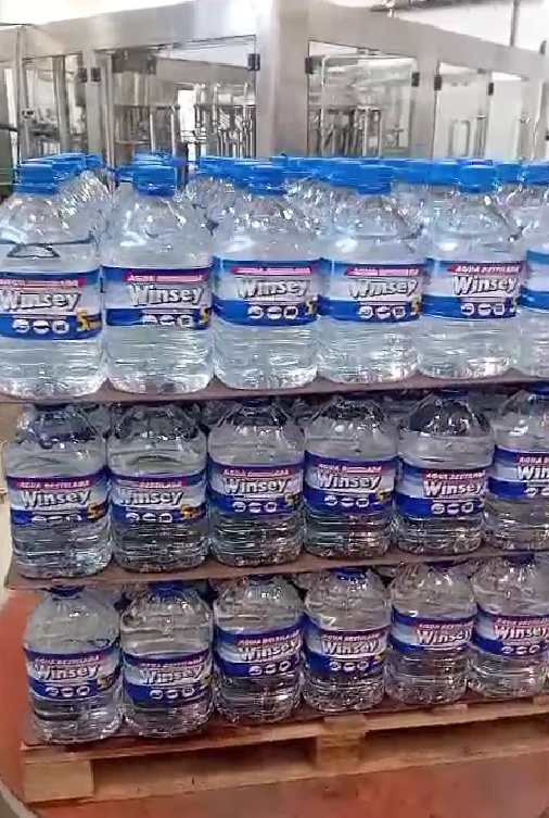 Palés apilados con garrafas de agua azules de 5 galones en un área de almacenamiento de un almacén.