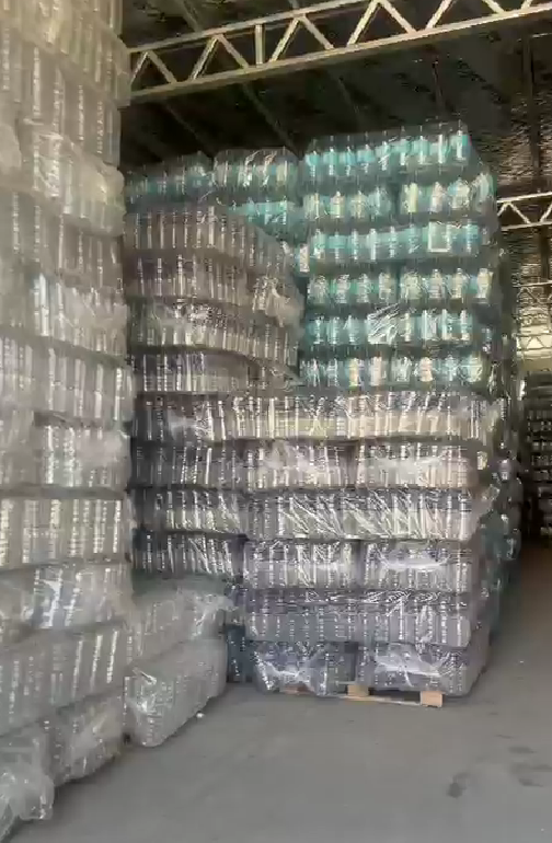 Interior de un almacén con filas de palés envueltos y maquinaria industrial junto a grandes ventanales.