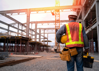 Construction worker in a reflective vest and hard hat at a steel-frame building site at sunset