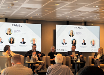 Panel discussion in a conference room, with speakers seated on stage and slides showing panelists behind them