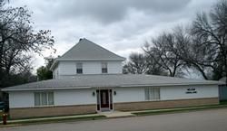 Small white office building with a front porch and a sign, under a cloudy sky