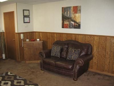 Living room with brown leather loveseat, wood paneling, wall art, and a closed door