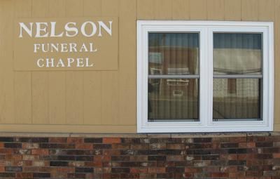 Nelson Funeral Chapel sign on tan building with brick base and white-framed window