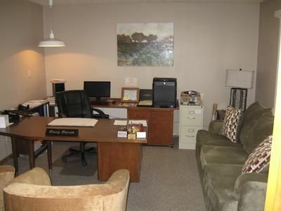 Small office with desk, computer, chairs, couch, and filing cabinets against beige walls.