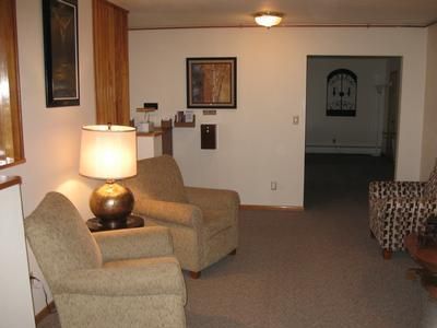 Cozy living room with two armchairs, a lamp, framed wall art, and a doorway to a darker room
