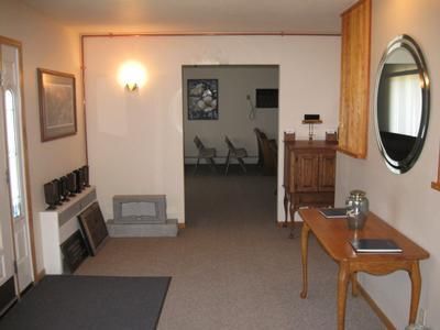 Narrow hallway with wall sconces, mirror, small table, and chairs visible in a room beyond.
