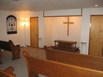 Small chapel interior with wooden pews, a cross on the wall, and a simple altar at the front.
