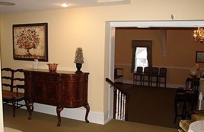 A view of a tan room with a wooden sideboard, framed artwork, and a staircase leading to a furnished interior space.