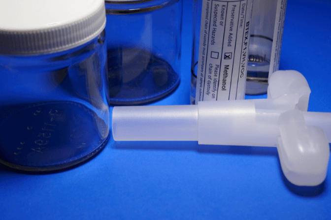 A jar with a white lid sits next to a syringe on a blue surface