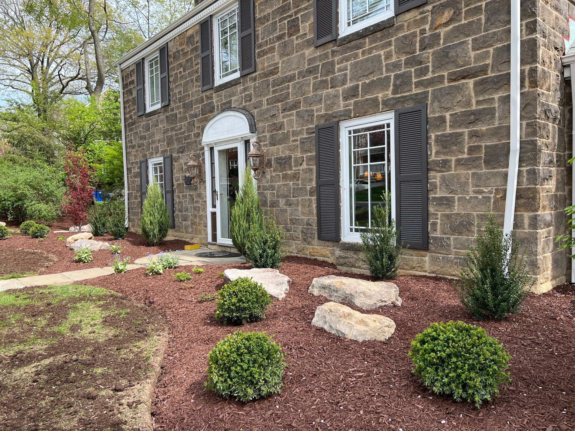 Stone house with white trim and landscaped front yard with shrubs and mulch beds
