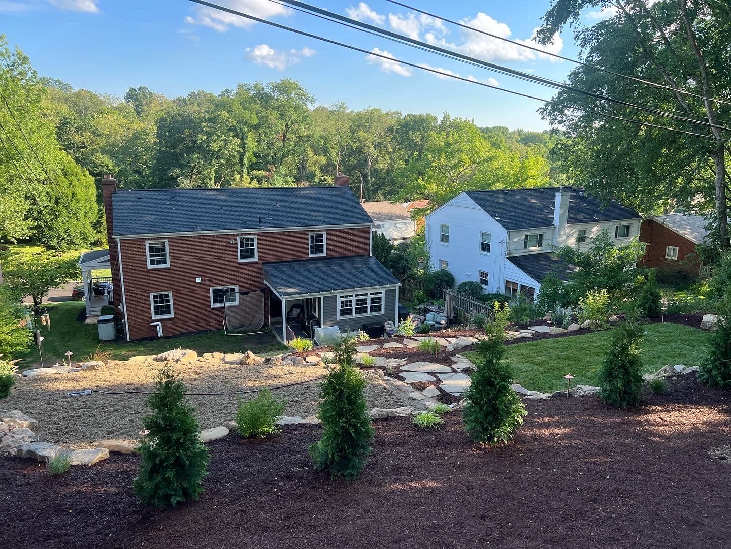 hill behind house with stone walkway, mulched garden beds with arborvitae trees