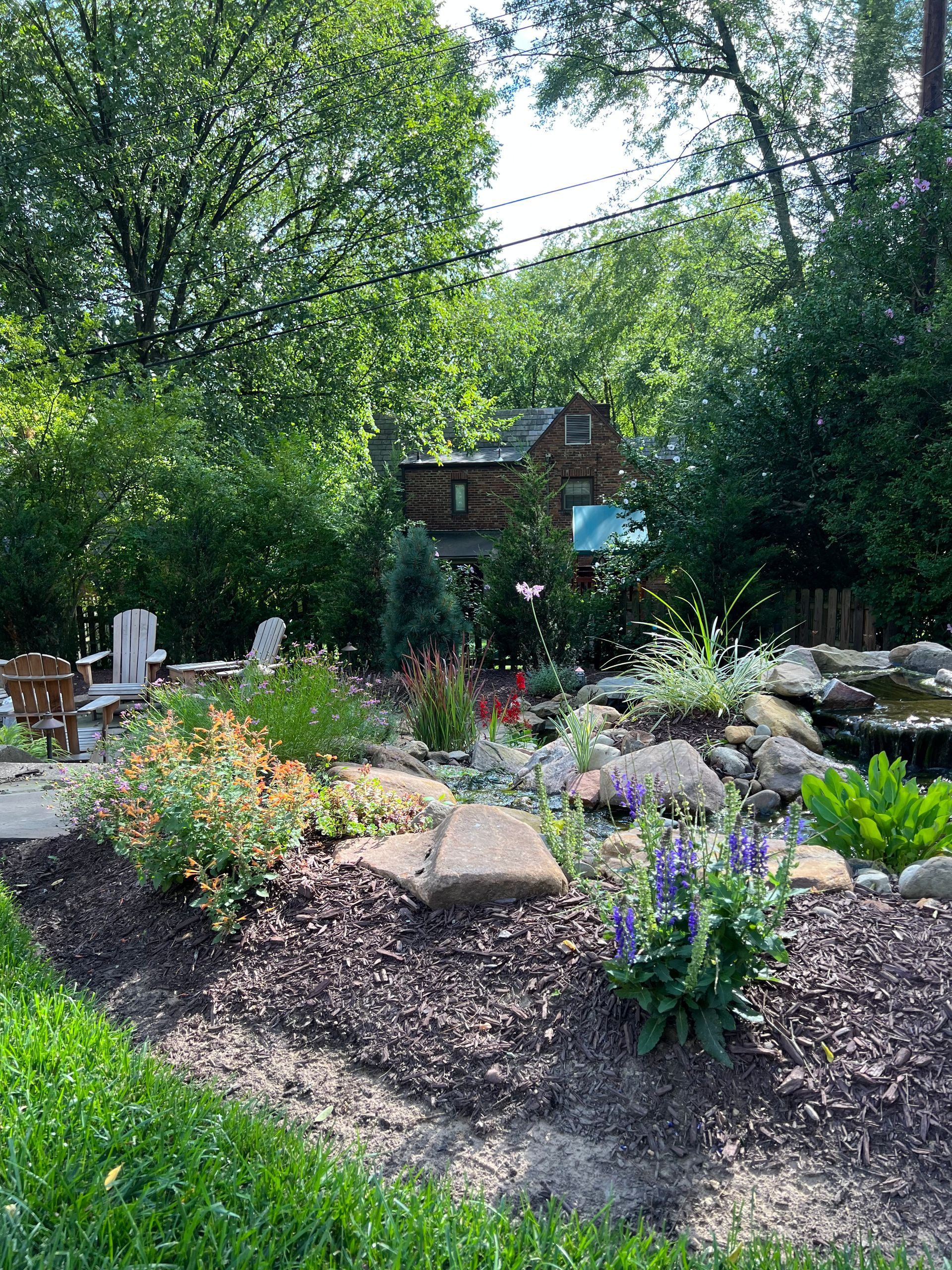 Colorful flower garden with stone path, lush greenery, and a small wooden shed in the background