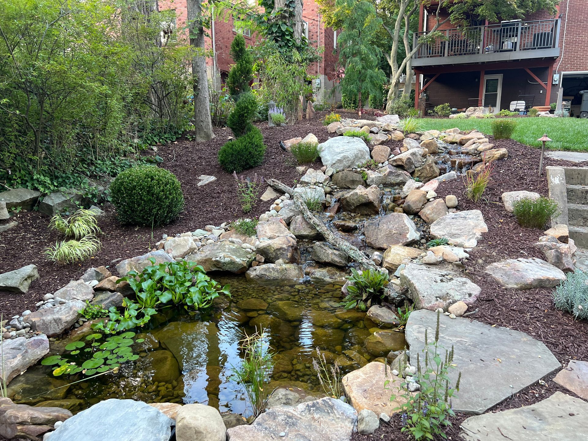 Rock garden with a small pond, stacked stones, and lush greenery in a landscaped yard