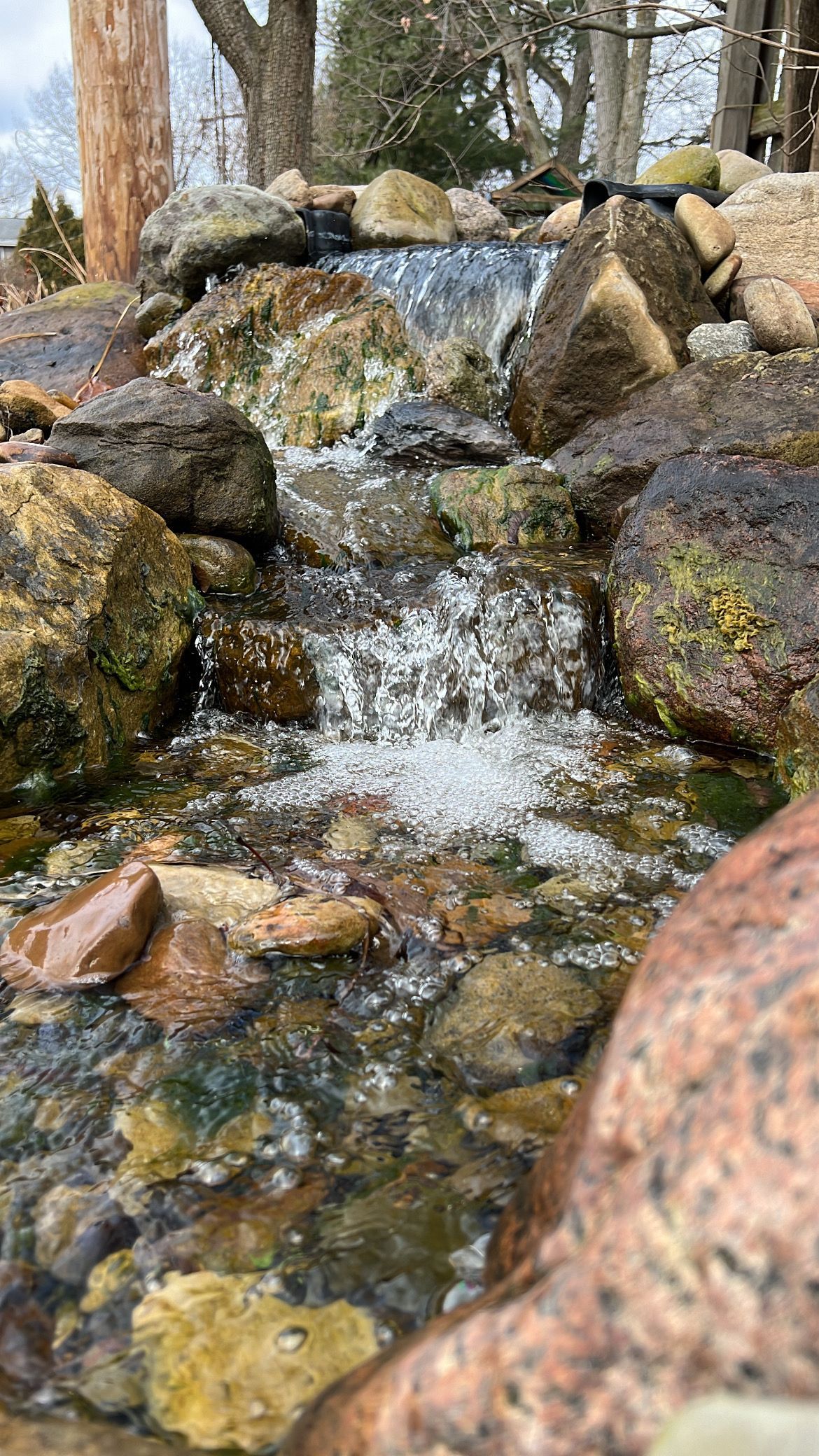 Small stream cascading over rocks in a wooded area, with water splashing through mossy stones.