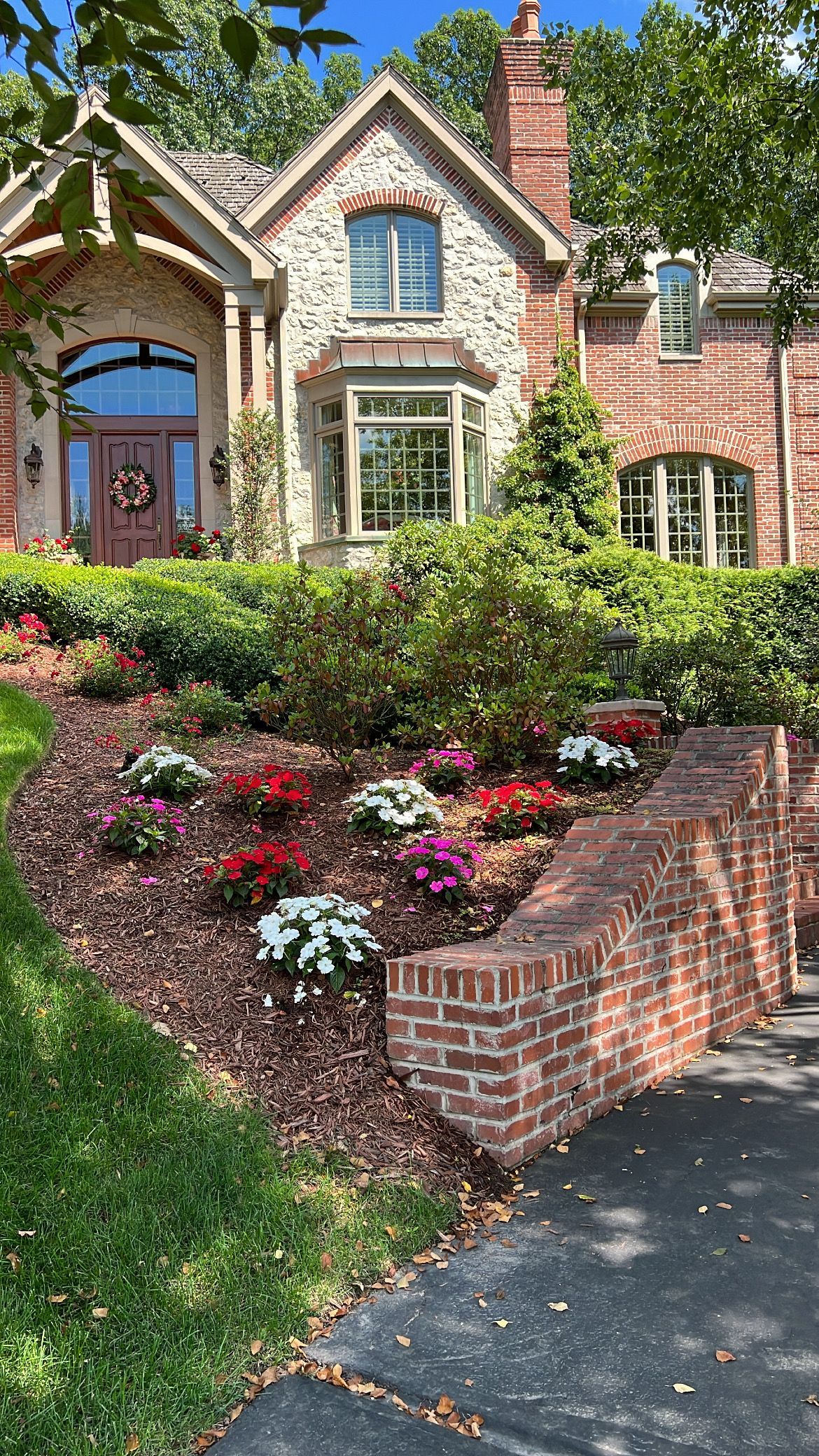 Brick cottage with a lush flower garden, arched gate, and driveway in front