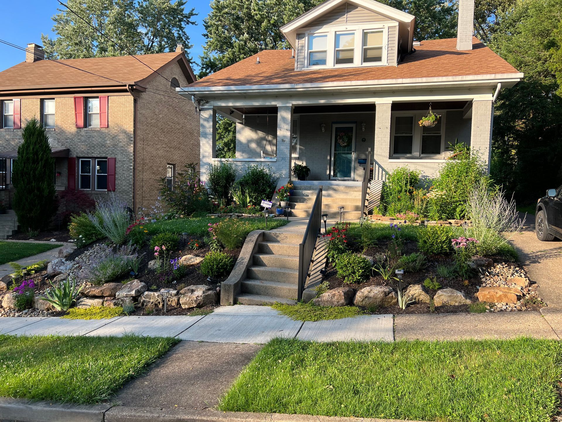 Suburban house with front porch, stone steps, and a landscaped flower garden in front of the lawn