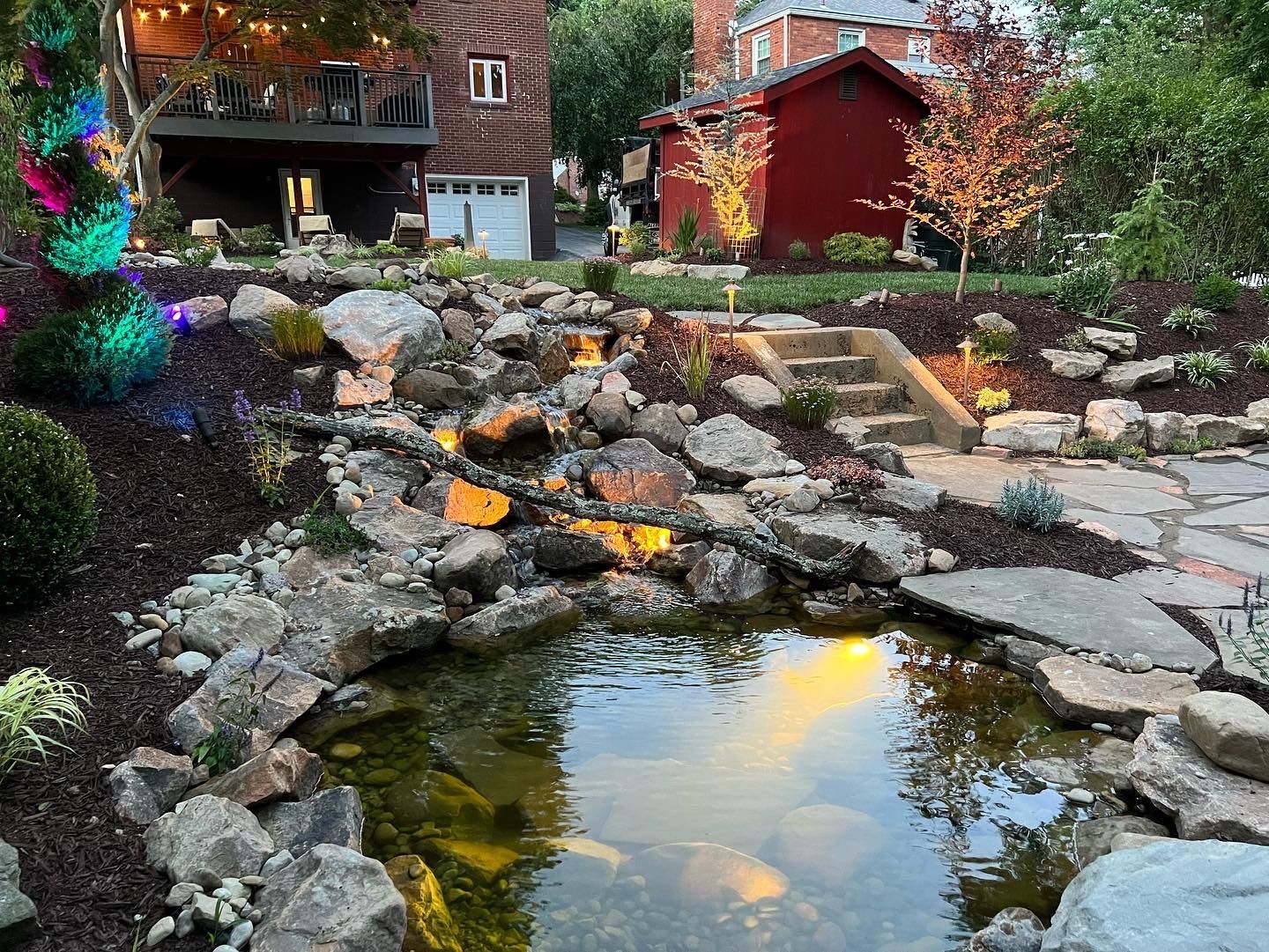 Backyard koi pond with rock waterfall, stone path, and autumn garden beside a red shed