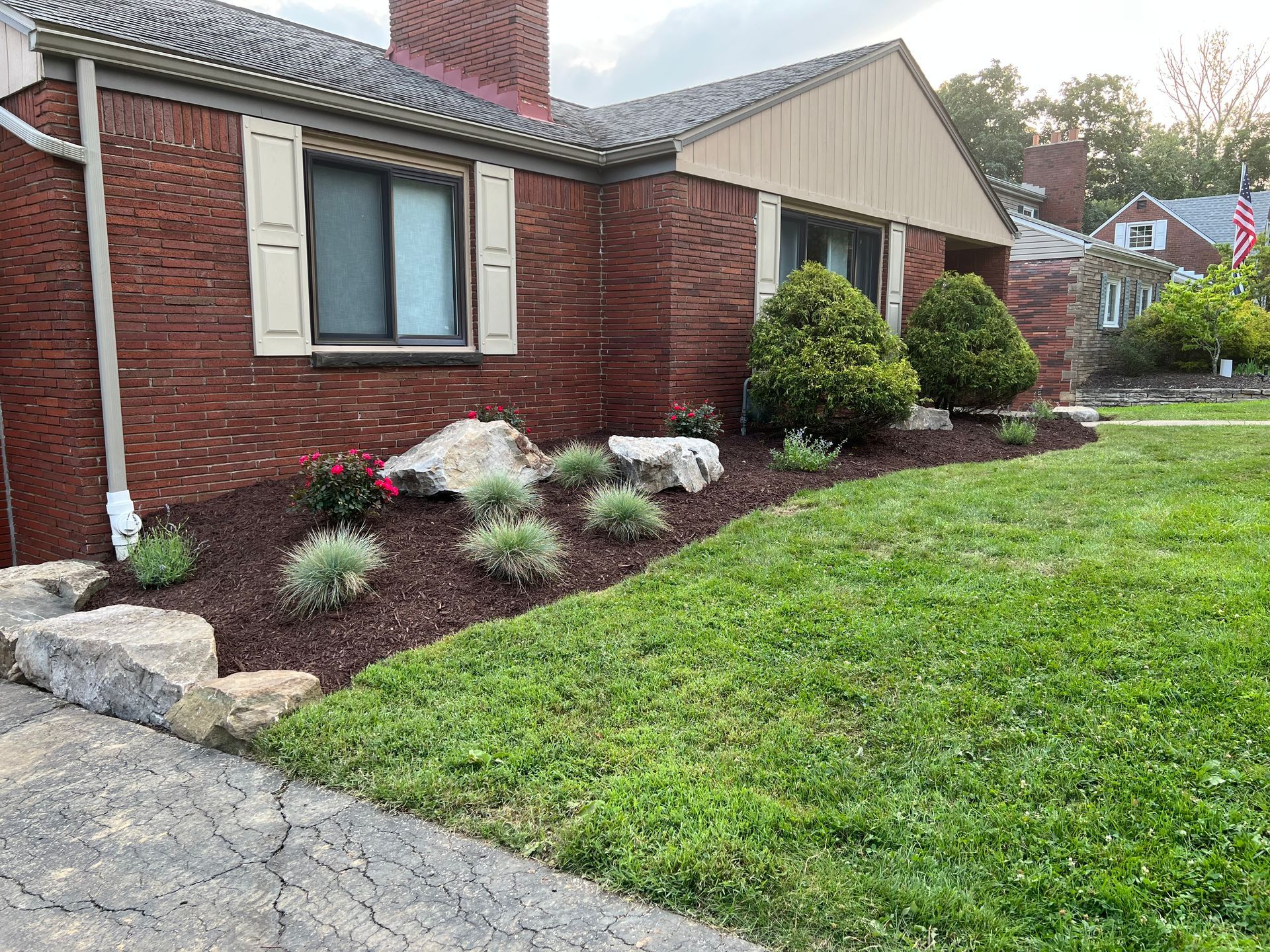 Front yard with red brick house, landscaped flower beds, and green lawn beside a paved driveway