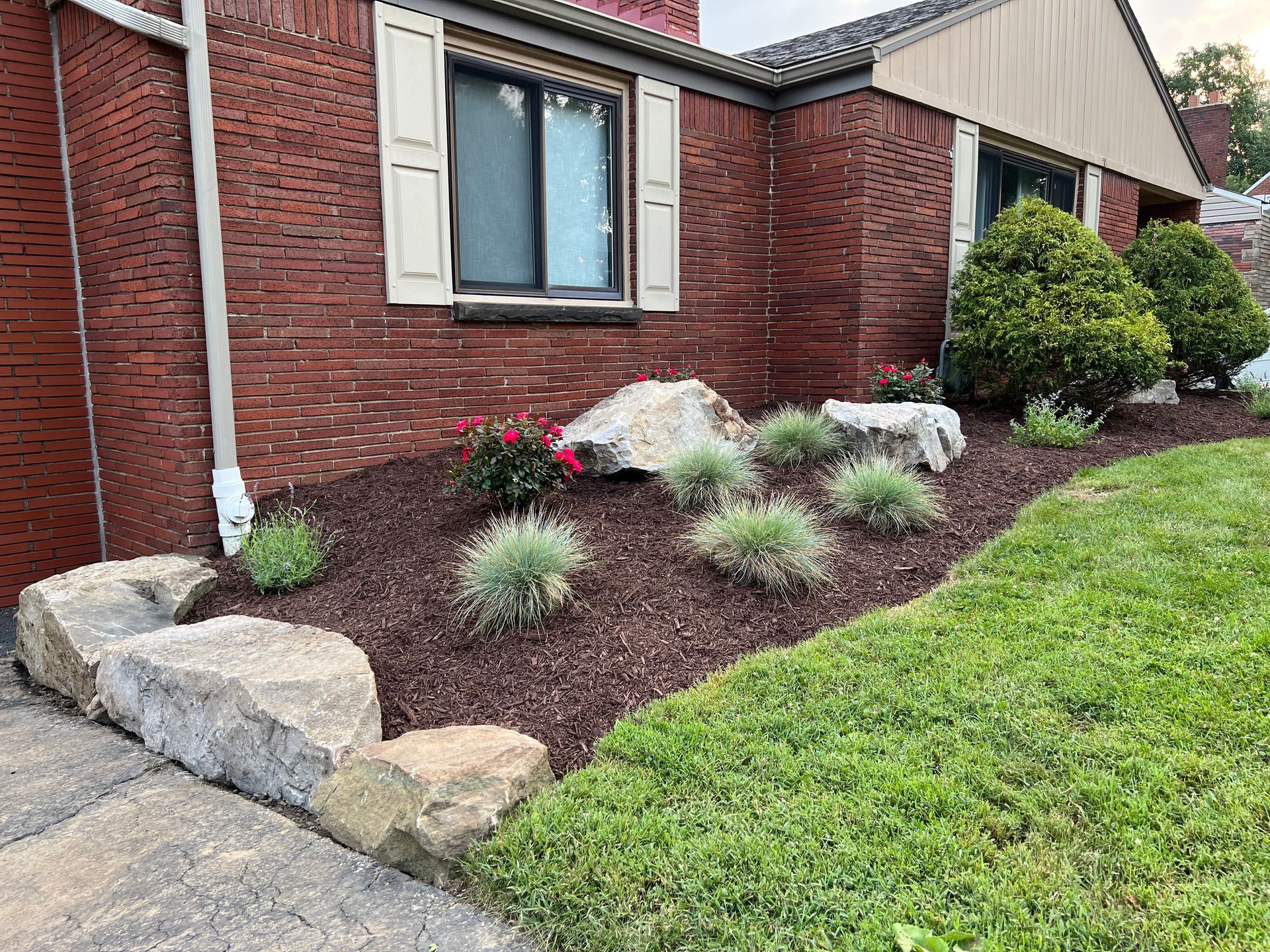Front yard landscaping with rocks, mulch, and small shrubs beside a brick house