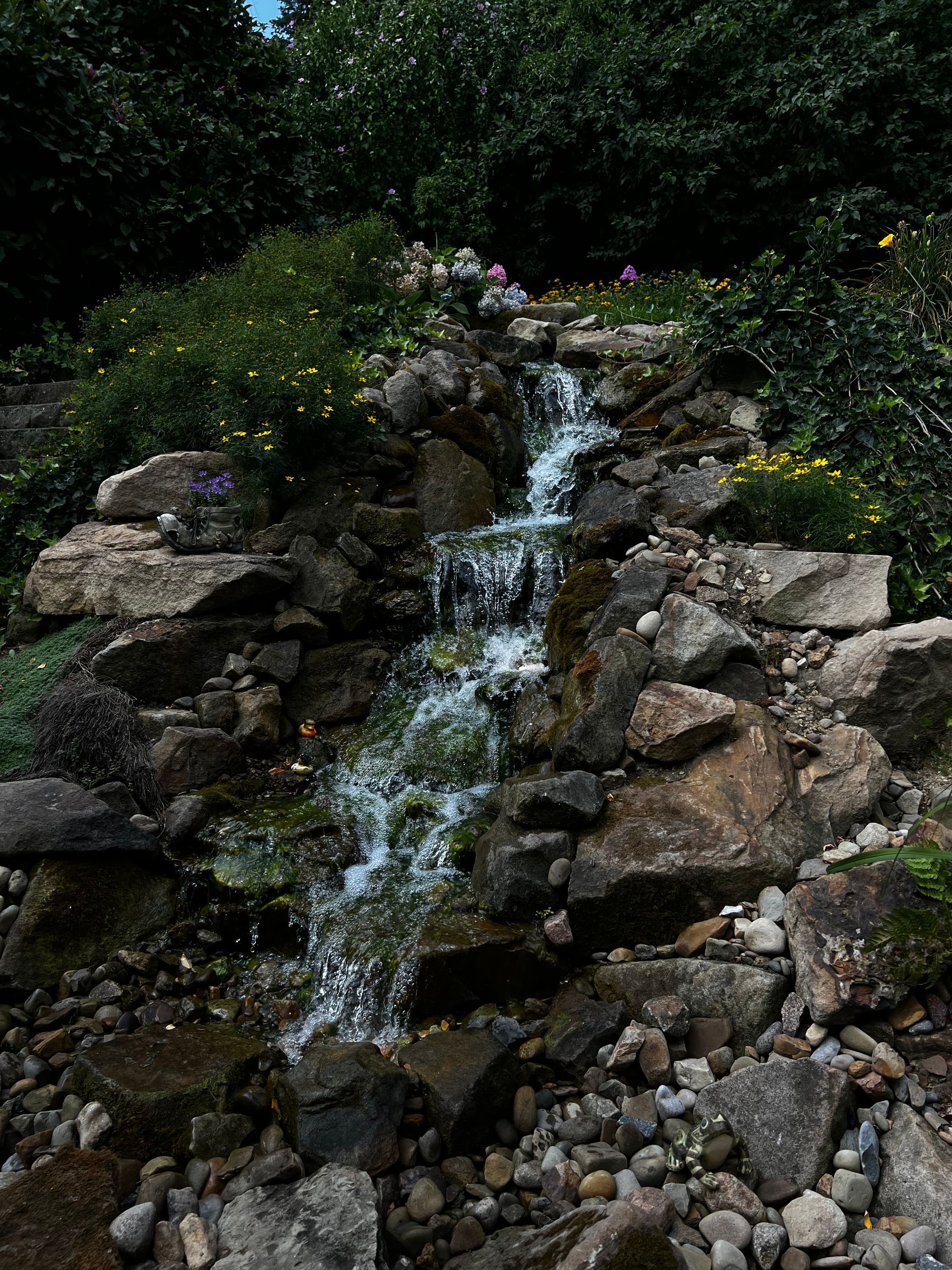 Small waterfall cascading over rocks in a landscaped garden with green foliage and flowers