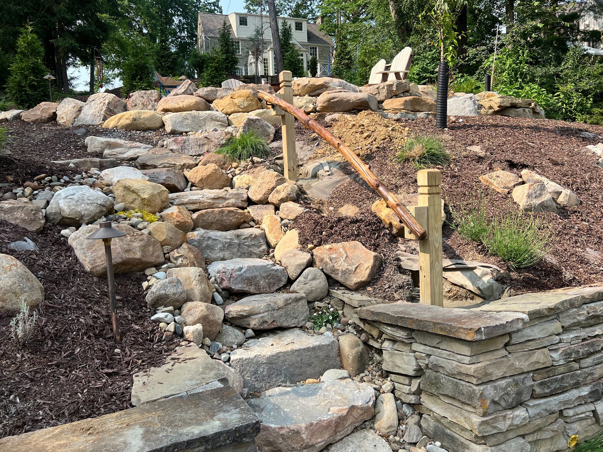 Stone steps and wooden handrails on a landscaped hillside garden with rocks and shrubs