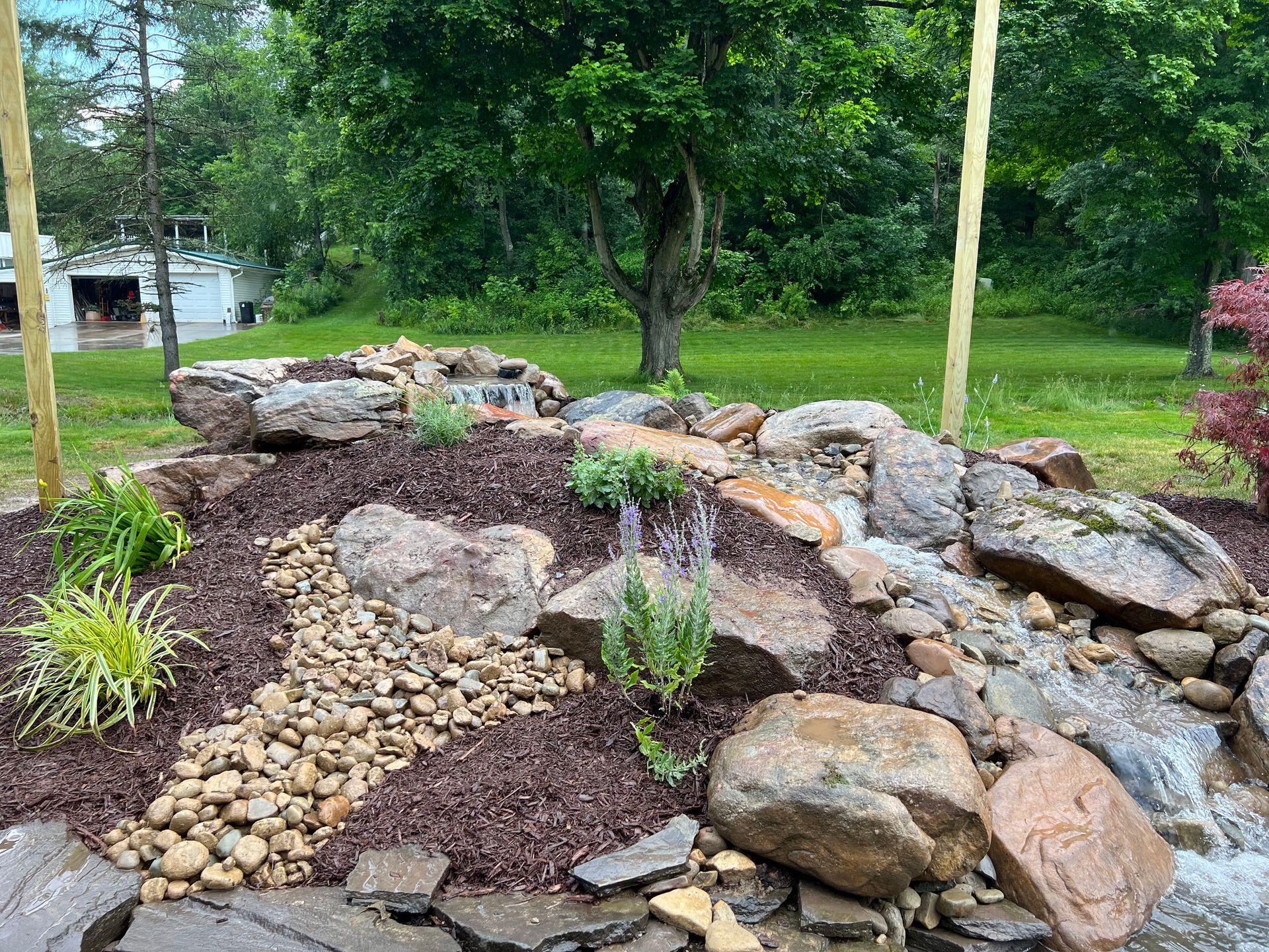 Rock garden with stacked stones, mulch, and small plants in a green yard