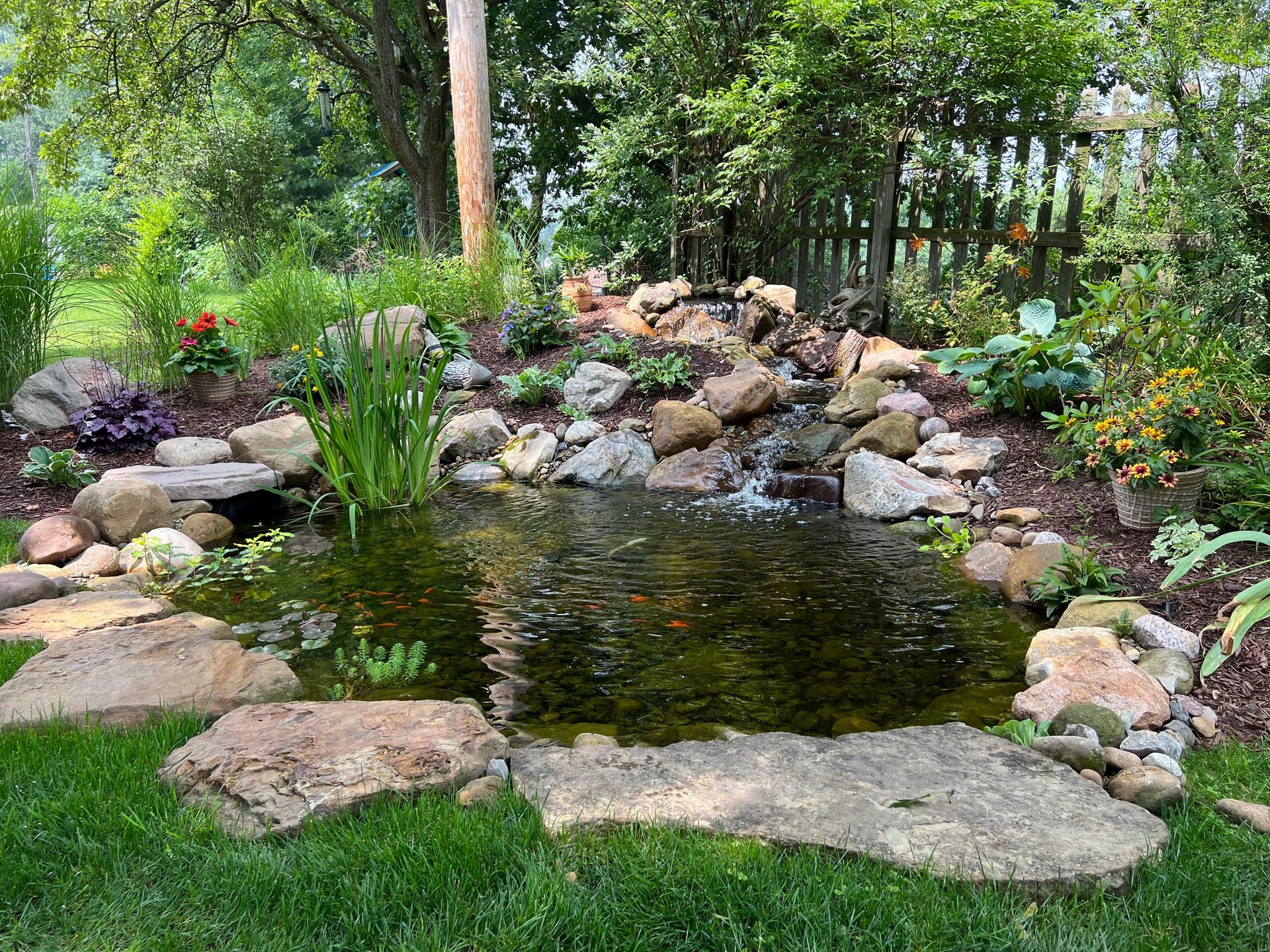 Rock garden pond with lily pads, surrounded by stones, flowers, and lush green trees