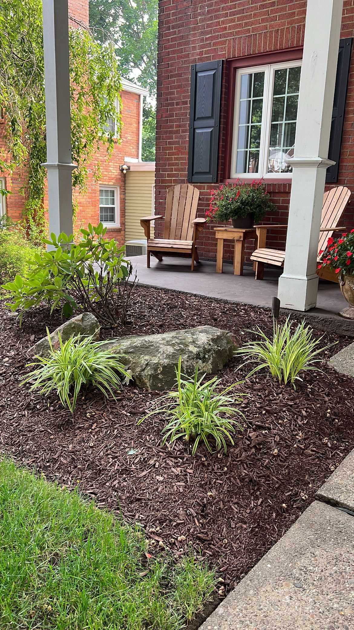 Brick patio with a chair, potted plants, and a small landscaped garden with rocks and mulch.