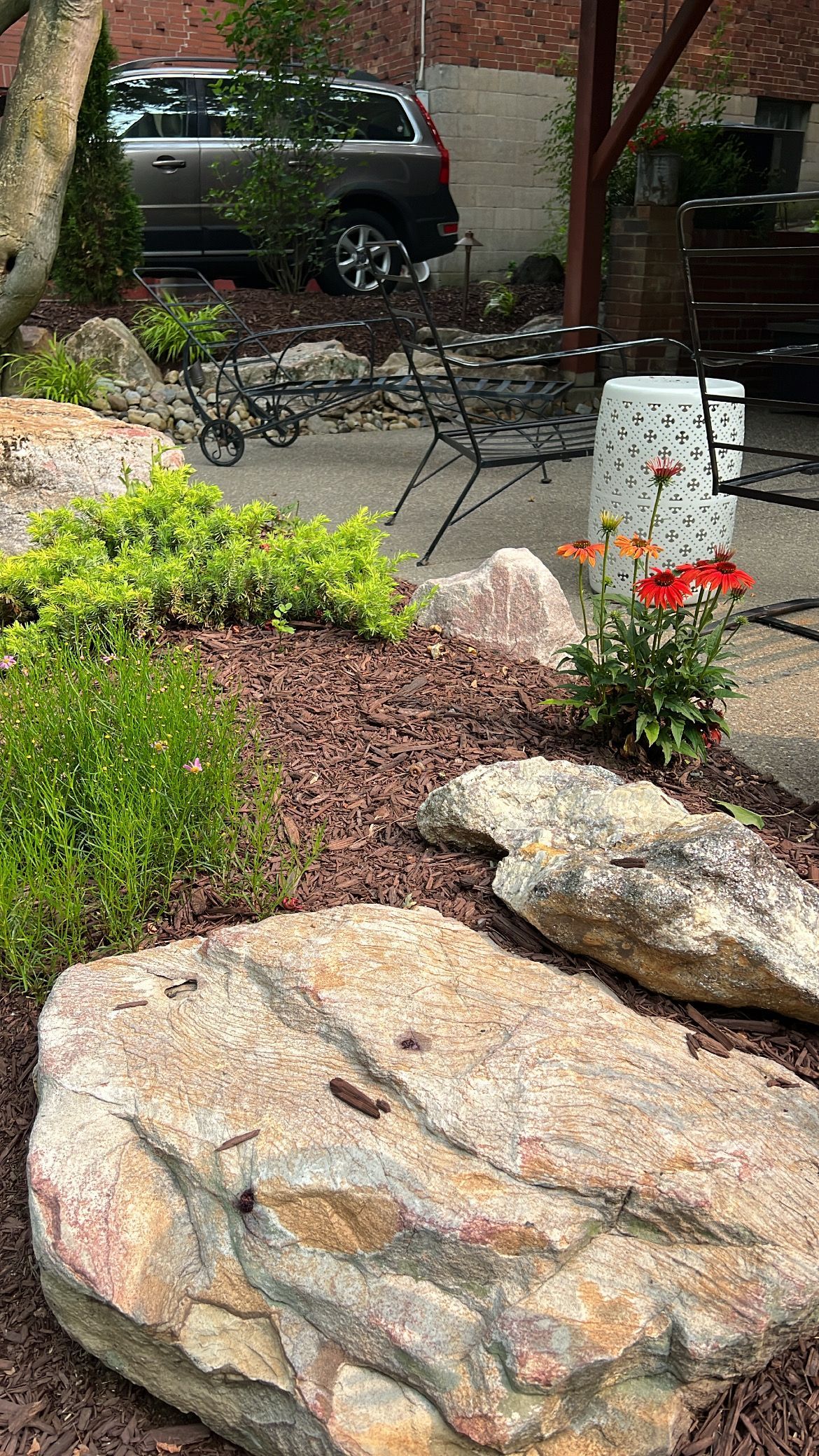 Rock garden with large boulders, red flowers, and a parked SUV in the background