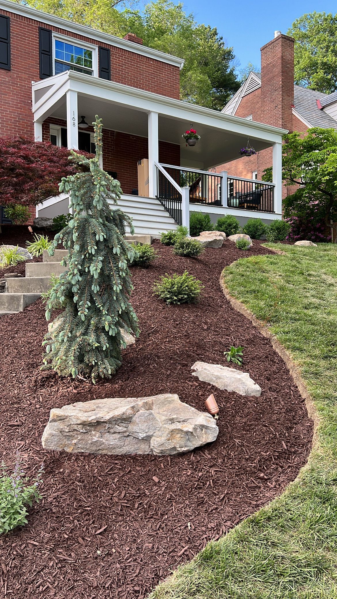 Front yard garden path with mulch, stepping stones, shrubs, and a house porch in the background