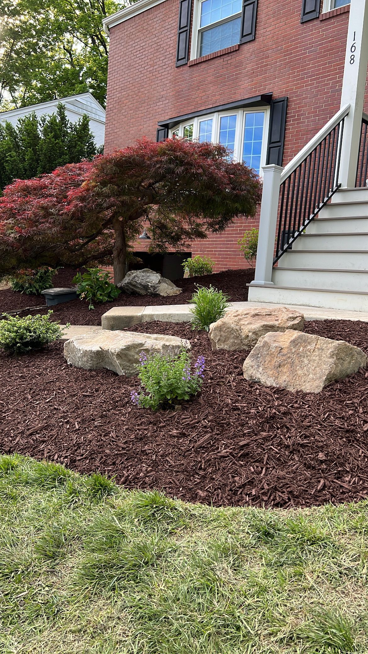 Front yard landscaping with shrubs, rocks, and stairs beside a brick house