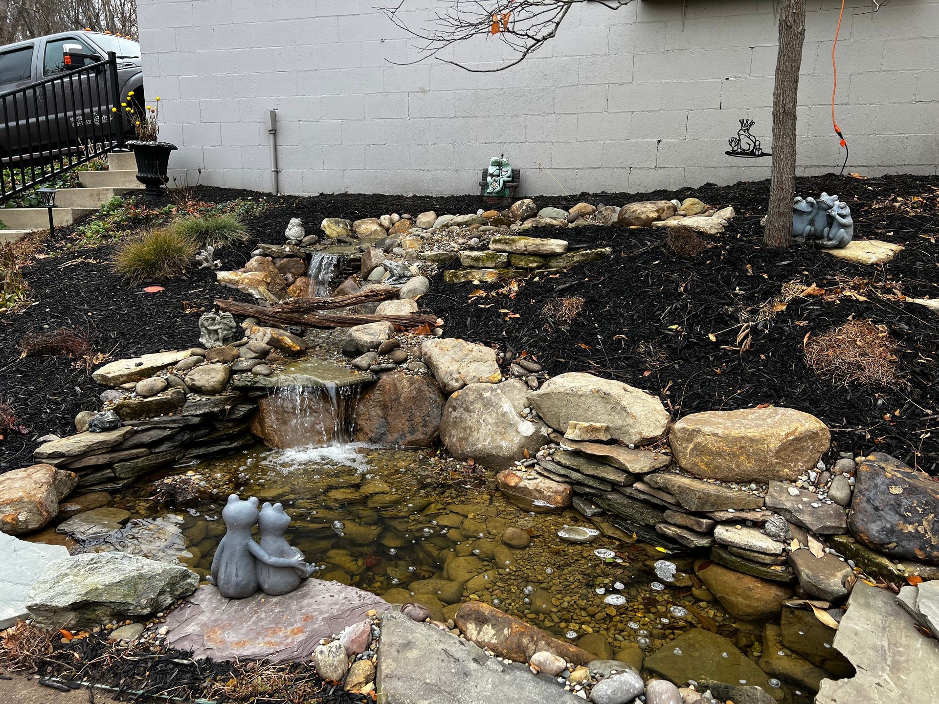 Backyard rock waterfall and koi pond with small gray cat statue in the foreground