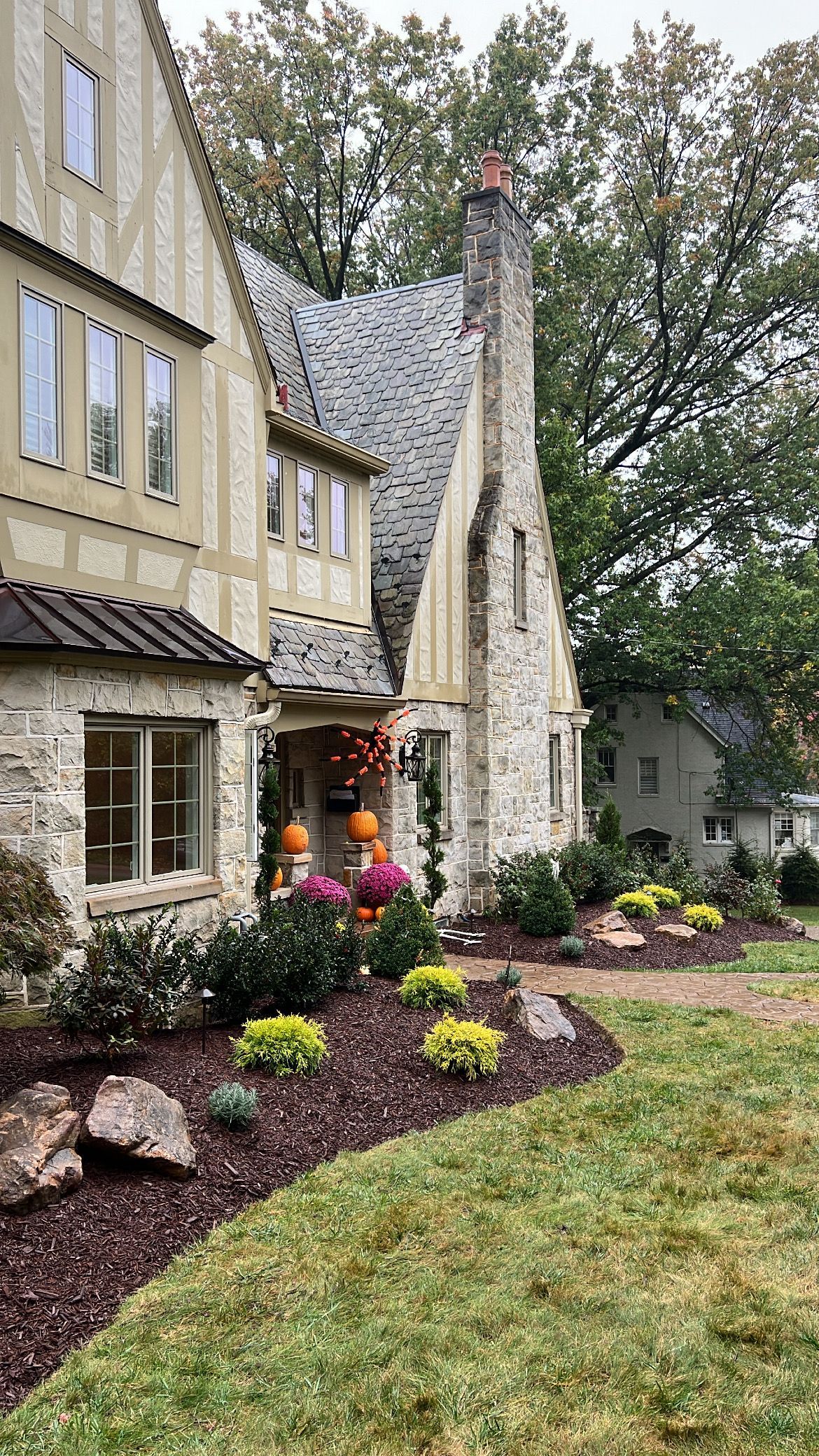 Stone building entrance with arched doorway, pink flowers, and landscaped garden beside a grassy yard.
