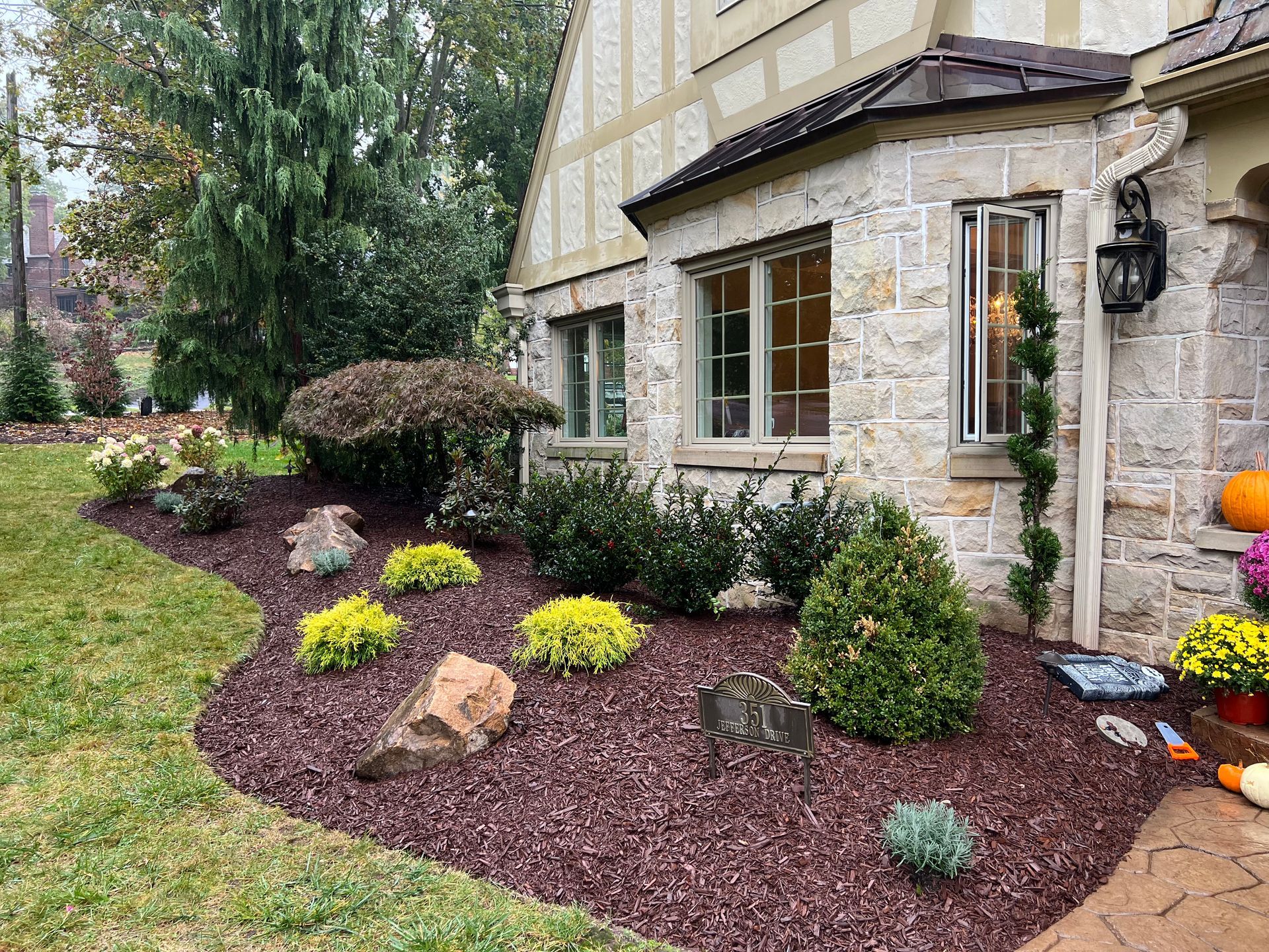 Stone house with a landscaped front yard, mulched flower beds, and small shrubs along the walkway