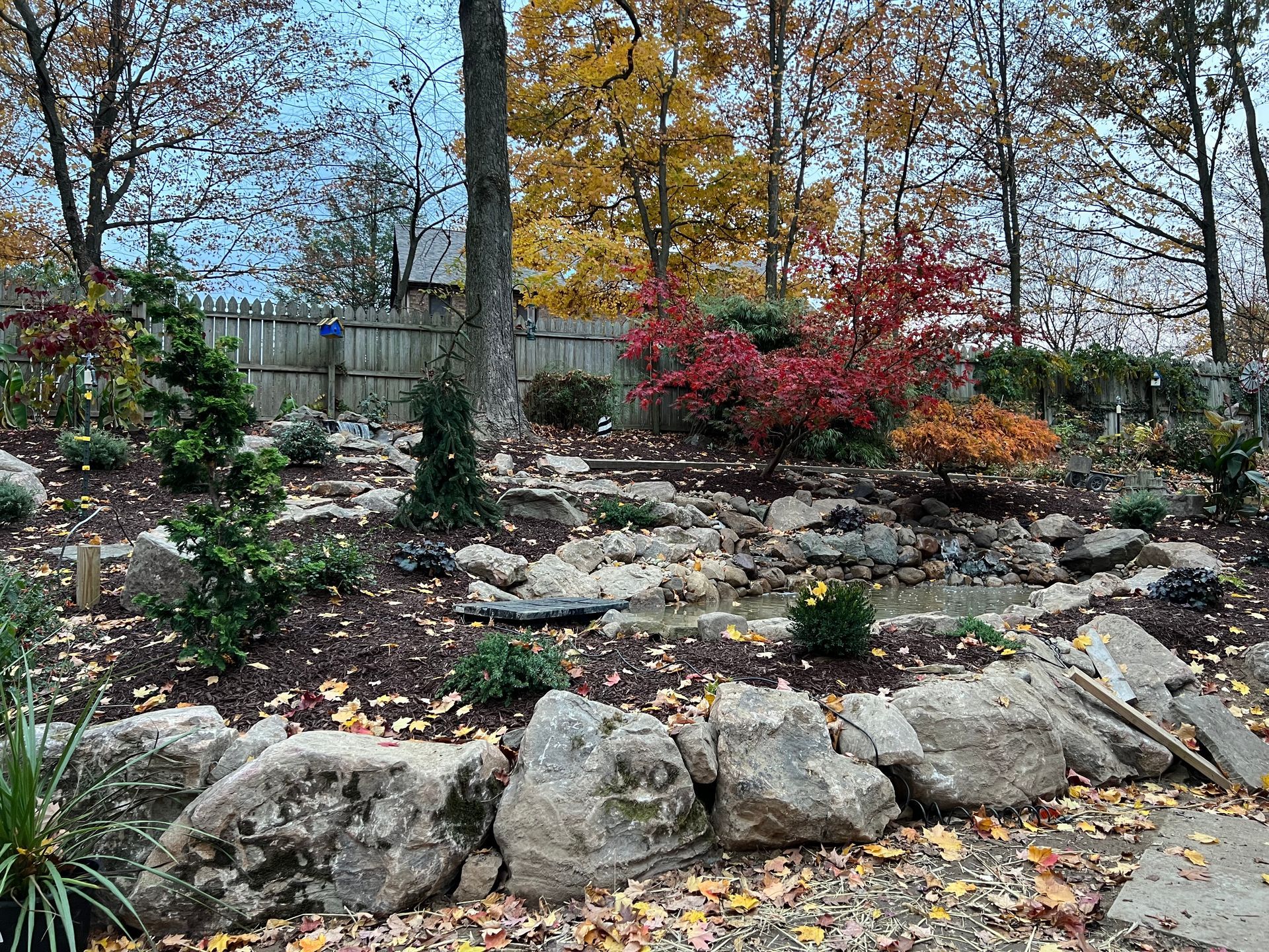 Landscaped rock garden with autumn shrubs and trees behind a stone border