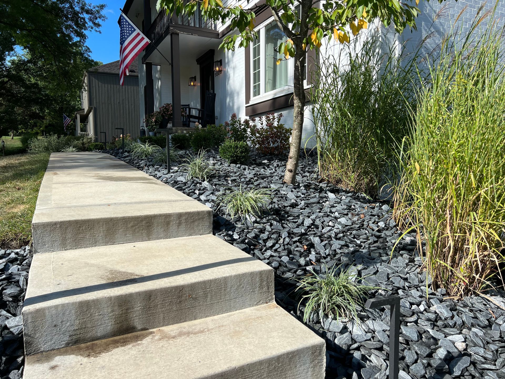 Concrete steps leading to a front porch with an American flag and landscaped gray rock garden