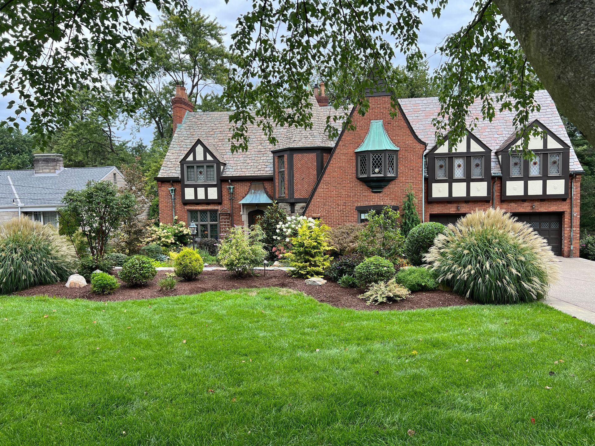 Brick Tudor-style house with red roof, manicured lawn, and colorful front garden