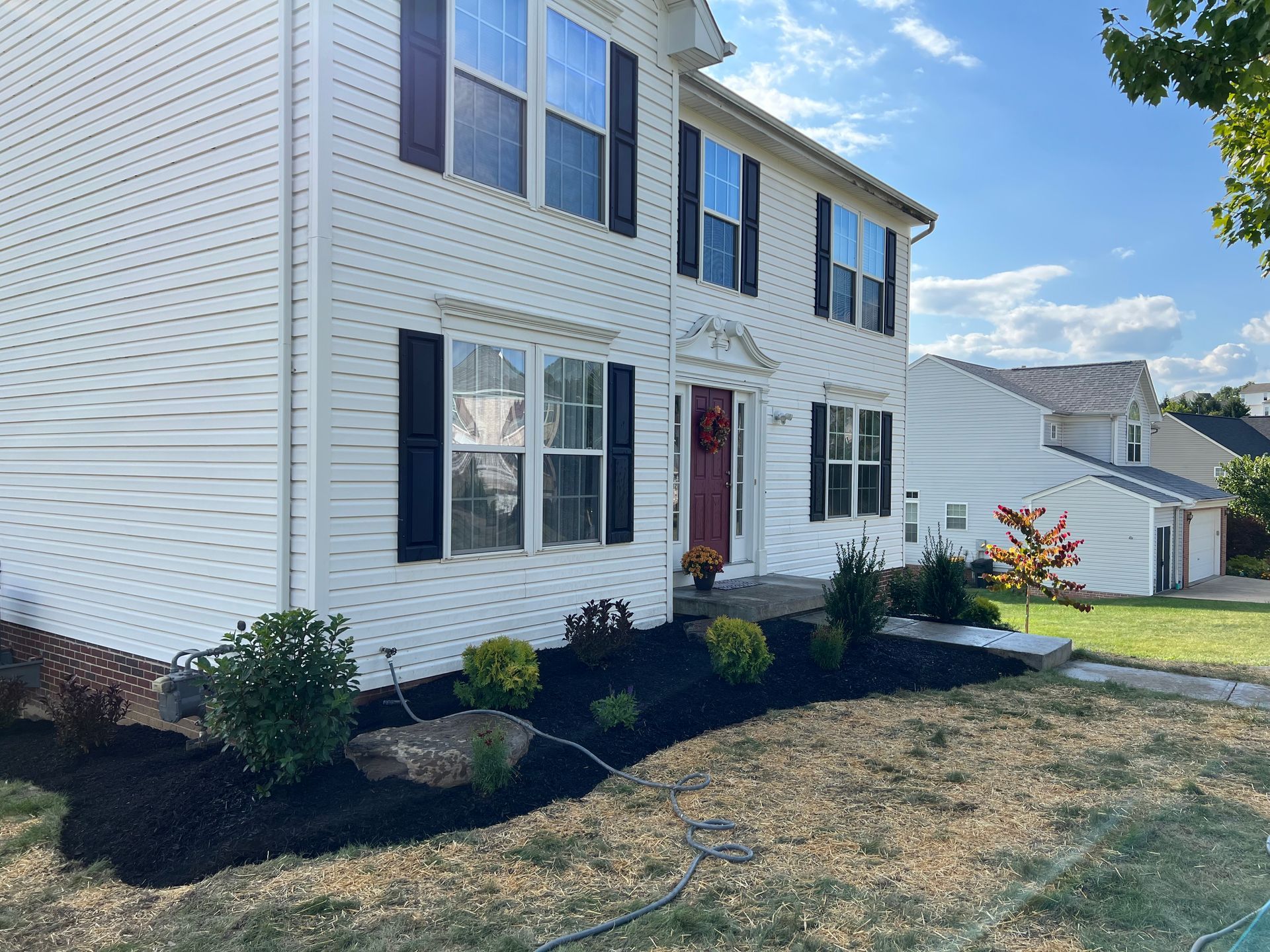 Two-story white house with black shutters, red front door, and landscaped front yard