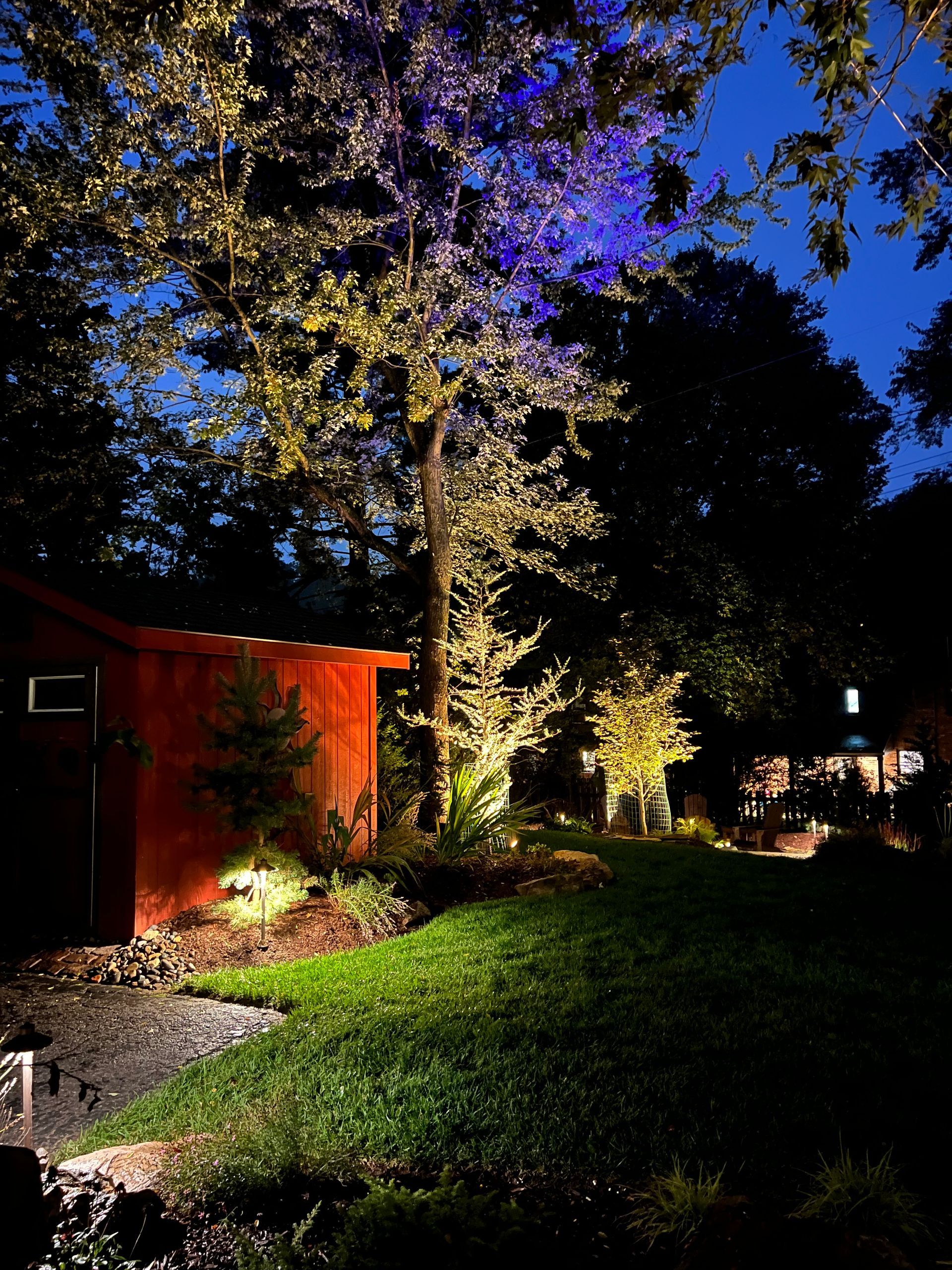 Nighttime garden with a lit tree, red shed, and illuminated grass path